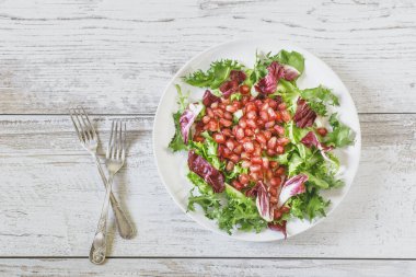 Sağlıklı vejetaryen salatası hindiba, karışık marul, roka ve beyaz tahta üzerinde nar.
