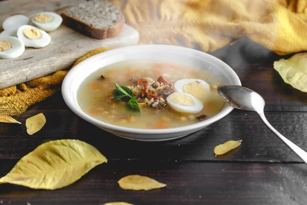 Healthy and warming winter soup with rice, carrot, chickpeas, chicken, ham and boiled egg over rustic wooden table background. Spanish soup (Puchero Andaluz). Winter food concept