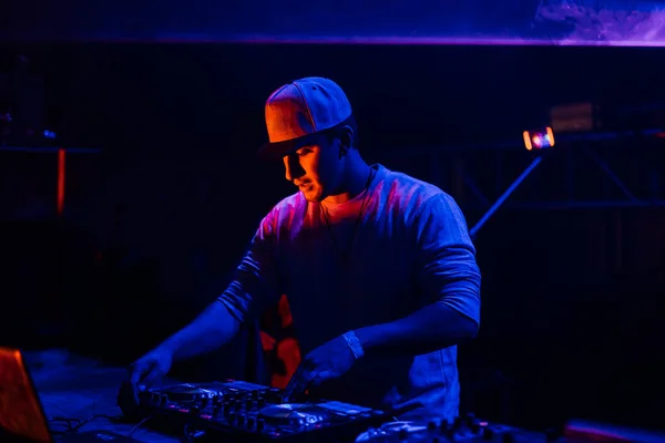 Gece partisinde mavi ve kırmızı ışıklar altında karışık müzik çalan genç bir DJ 'in portresi. Eğlence, gençlik, eğlence ve festival konsepti. 