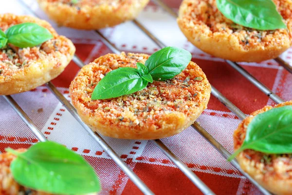 Domates, kekik ve fesleğenle pişirilmiş Mini pizzaları kırmızı ve beyaz kareli masa örtüsüne yakın..