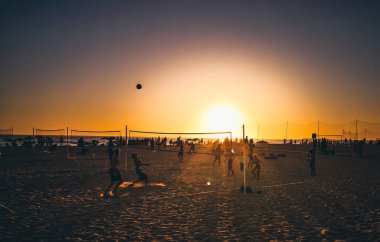 Cadiz, İspanya - 3 Ağustos 2023: La Victoria Plajı, genç insanlar sıcak günbatımı ışığında kumsalda voleybol oynuyorlar. Playa Victoria, Cadiz 'in batı yakasında, Costa de la Luz' da yer alan bir şehir plajı..