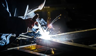 Profesyonel maskeli kaynakçının portre görüntüsü. Parlak elektrikli meşale demiri yakar.