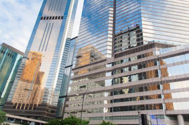 Hong Kong 'un merkezindeki modern ofis binaları. Gökyüzünü ve bulutları yansıtan pencereli modern mimari.