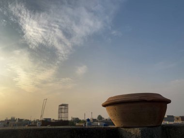 Mud water pot placed on the top of roof wall. Bird water feeder utensils with sunlight and a cloudy sky in the background. clipart