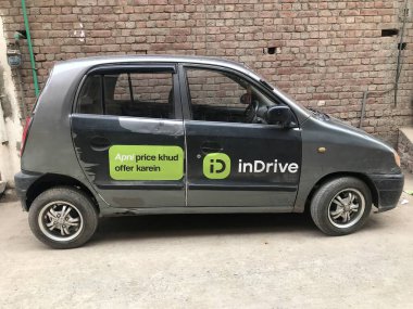 InDrive online Taksi veya Taksi Lahore şehrinin içindeki tuğla duvarın önünde park halinde..
