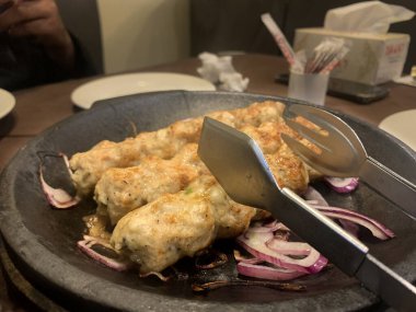 Seekh Kebap 'ın kıymalı tavuk ya da kuzu pirzolasından yapılmış, sıcak tavada soğanla servis edilmiş yan görüntüsü..
