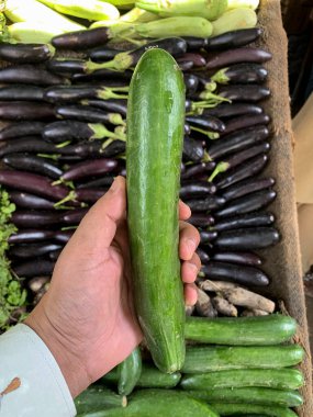 Sebze arka planında salatalık tutan bir erkek. Çocuk sol elinde salatalık tutuyor. Şehir: Lahor, Pakistan.