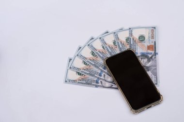 Cep telefonunun altına Amerikan dolarları ya da banknotlar yerleştirilmiş. Beyaz bir arkaplanda izole edilmiş.