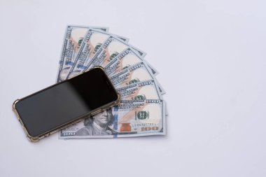 Cep telefonunun altına Amerikan dolarları ya da banknotlar yerleştirilmiş. Beyaz bir arkaplanda izole edilmiş.