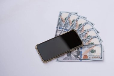 Cep telefonunun altına Amerikan dolarları ya da banknotlar yerleştirilmiş. Beyaz bir arkaplanda izole edilmiş.