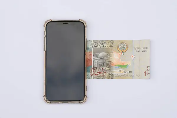 stock image 1 Kuwait Dinar bill or bank notes placed under mobile phone. Isolated on a white background. Kuwaiti Dinar country paper currency.