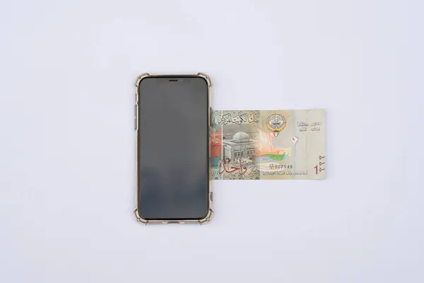 stock image 1 Kuwait Dinar bill or bank notes placed under mobile phone. Isolated on a white background. Kuwaiti Dinar country paper currency.