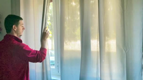 男の子は外を見るために家の窓のカーテンを開きます — ストック動画