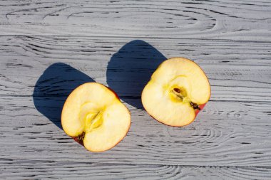 Olgun kırmızı elmanın iki yarısı gün boyunca açık ahşap bir zeminde yatar..