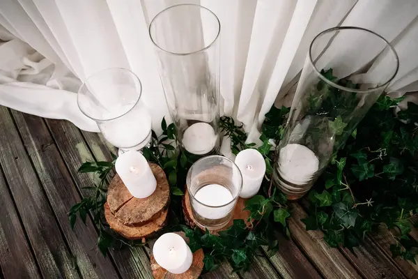 用白色桌布装饰节日餐桌 从玻璃瓶中的蜡烛 站在木制看台上 地板上 餐厅里 它们周围是新鲜的叶子 — 图库照片