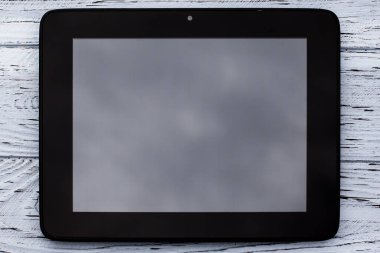 A black tablet with a blank display without an image lies on a light wooden textured surface