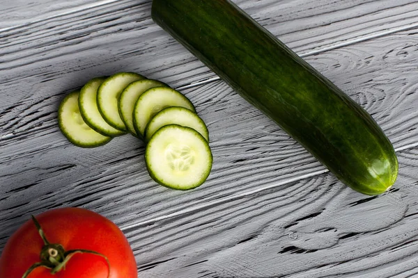 stock image Composition of whole and sliced ripe cucumbers and tomato, on a wooden light textured table, in the kitchen. Image for your creativity and design or decorations.