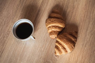 Lezzetli kruvasanlarla, açık kahverengi desenli ahşap bir masada, bir fincan sıcak kokulu siyah kahve..