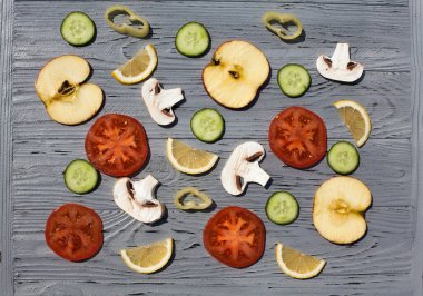 Taze kesilmiş sebze ve meyve kompozisyonu. Şampiyonlar, limon, biber, elma, salatalık ve domatesler açık ahşap bir arka planda uzanır..
