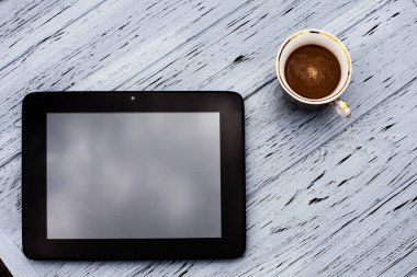 Bir bardak aromatik sade kahve ve açık ahşap bir masada siyah bir tablet..