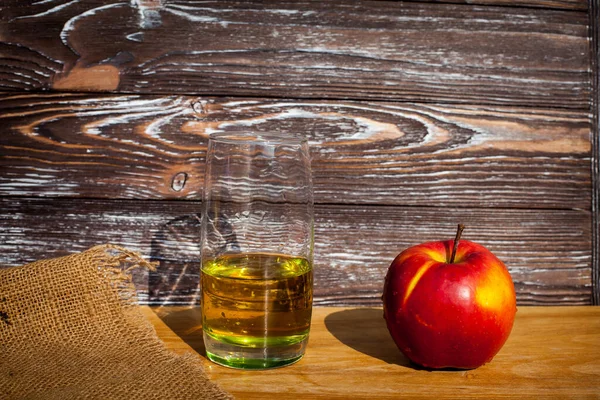 木の質感の壁に布で覆われたテーブルの上に新鮮な絞りリンゴジュースと赤い熟したリンゴのガラス — ストック写真