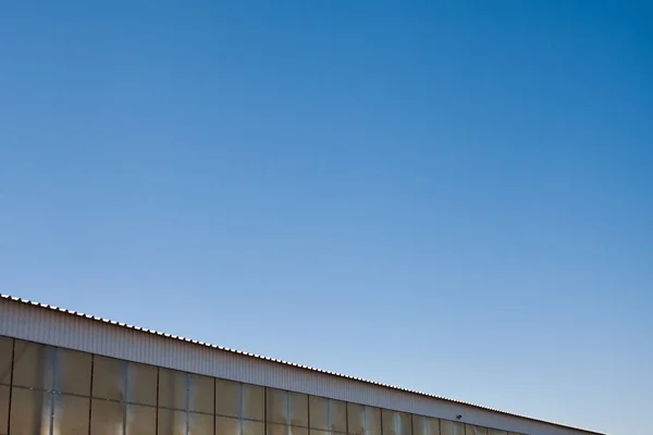 stock image The upper part of an industrial building against the backdrop of a blue clear sky during the day. Background image for your design or illustrations.