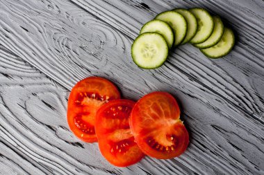 Mutfaktaki ahşap bir masada dilimlenmiş domates ve salatalıktan oluşan iştah açıcı bir kompozisyon..