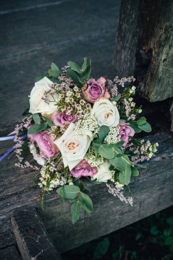 Güzel, şık bir buket pembe ve beyaz gül, ahşap bir bankta uzanıyor, koyu bir arka planda..