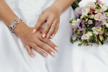 Beyaz gelinlikli şık bir gelin. Yakınlarda renkli çiçeklerden oluşan şık bir buket var..