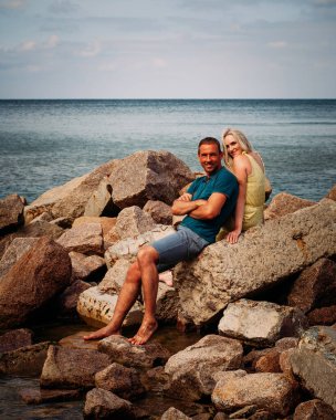 Birbirine aşık bir çift okyanusun yakınındaki kayalıklarda oturur ve gülümser. Mavi kot şortlu, mavi tişörtlü, esmer bir adam. Güzel bir kız sarı tulum giymiş..