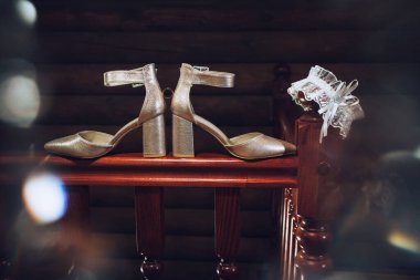 Sanat eserleri. Düğün aksesuarları, fildişi renkli kadın şenlik ayakkabıları, altın alyansları, kahverengi korkuluklarda beyaz bir jartiyer, karanlık bir odada bir dairenin içinde..
