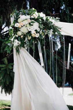 Gelin ve damat için şenlikli düğün kemeri, canlı taze çiçekler, cam kolyeler ve beyaz kumaşlarla süslenmiş, ağaçların arka planında, sokakta, evlilik töreni için..