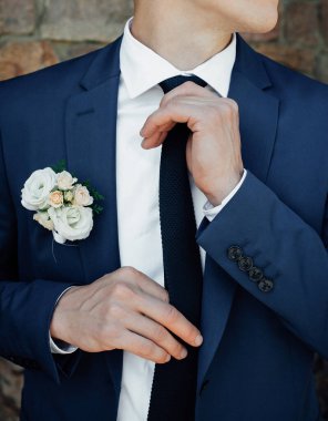 Mavi takım elbiseli, siyah kravatlı, beyaz gömlekli şık bir damat kravatını düzeltir ve yana bakar. Düğün günü için sabah hazırlıkları.