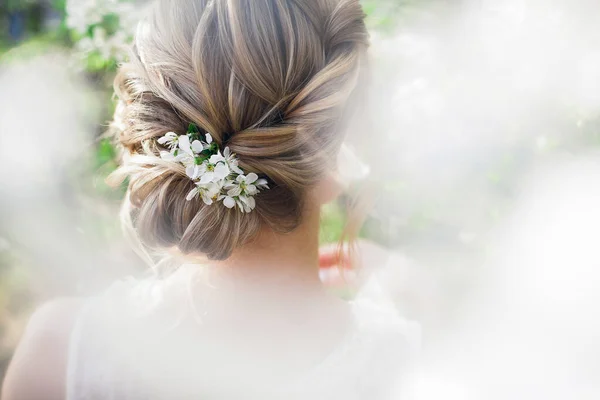 Art work hairstyles with weaving for a blonde bride in a blooming spring garden with green leaves