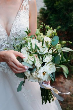 Yüzü olmayan bir tatilde sokakta yakası açık bir elbise içinde beyaz ve süt güllerinden oluşan güzel bir gelinin elinde büyük bir düğün buketi.