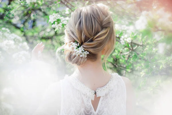 Art work hairstyles with weaving for a blonde bride in a blooming spring garden with green leaves