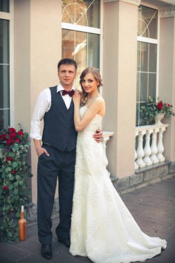 Sanat eserleri. Yeni evliler şık bir şekilde restoranın arka planına sarılıyorlar. Gelin hafif bir gelinlik giyiyor, damat beyaz gömlek, kazak ve papyon giyiyor..