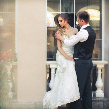 Güzel yeni evliler şık bir restoranın içinde. Beyaz gelinlikli gelin pencerede oturur, damat yanında durur ve kızı omzundan tutar..