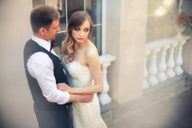 Sanat eserleri. Yeni evliler şık bir şekilde restoranın arka planına sarılıyorlar. Gelin hafif bir gelinlik giyiyor, damat beyaz gömlek, kazak ve papyon giyiyor..