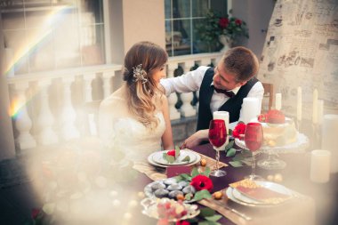 Sanat eserleri. Güzel, yeni evliler şık kıyafetler içinde düğün masasında oturuyorlar. Restoranın arka planında oturuyorlar..