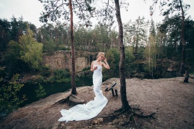 Sanat eserleri. Uzun beyaz kumaşa sarılmış zarif saç stili olan ince, güzel bir kadın gölün yukarısındaki pitoresk bir uçurumun kenarında çam ağaçlarının arasında duruyor..