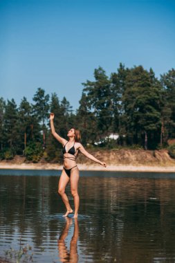 Uzun sarı saçlı ince bir kız ve siyah mayo giymiş spor bir figür, sıcak bir yaz gününde, denizde, denizde duruyor..