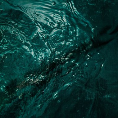 A dark green fabric with folds lies underwater with waves and splashes. Image for your creative design or stylish illustrations.