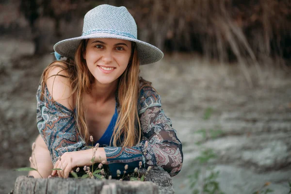 stock image Portrait of an attractive young smiling girl with long blond hair and a sporty figure, in a sexy blue swimsuit, a small hat and a blue summer shirt, stands in nature.