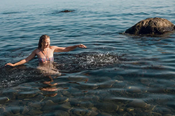 在一个阳光灿烂的日子里 一个金发碧眼 身穿条纹泳衣的女孩在海里洗澡 — 图库照片