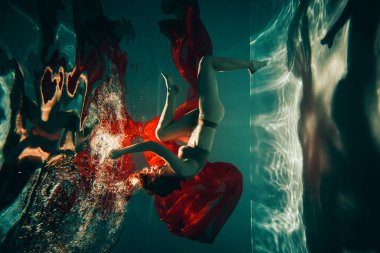 Sanat eserleri. Havuzda güzel röfleli kırmızı kumaşla iç çamaşırlı bir kızın sualtı çekimi..