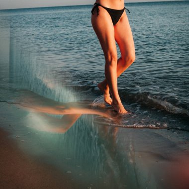 Sanat eserleri. Güzel atletik bacakları olan bir kız deniz kıyısında dalgalar boyunca yürüyor. Suda yansıması olan resim.