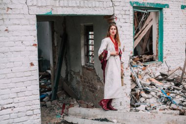 Art work on the theme of the war in Ukraine. A frustrated Ukrainian woman in national clothes and a bag in her hands stands near the ruins of a building bombed by the Russian army.