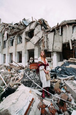 Art work on the theme of the war in Ukraine. A frustrated Ukrainian woman in national clothes and a bag in her hands stands near the ruins of a building bombed by the Russian army.