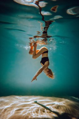 Sanat eserleri. İnce, bronz tenli, atletik vücutlu, sarı saçlı, siyah iç çamaşırlı, havuzda dalıp dönen bir kız. Tasarım ve dekorasyonunuz için estetik resim.